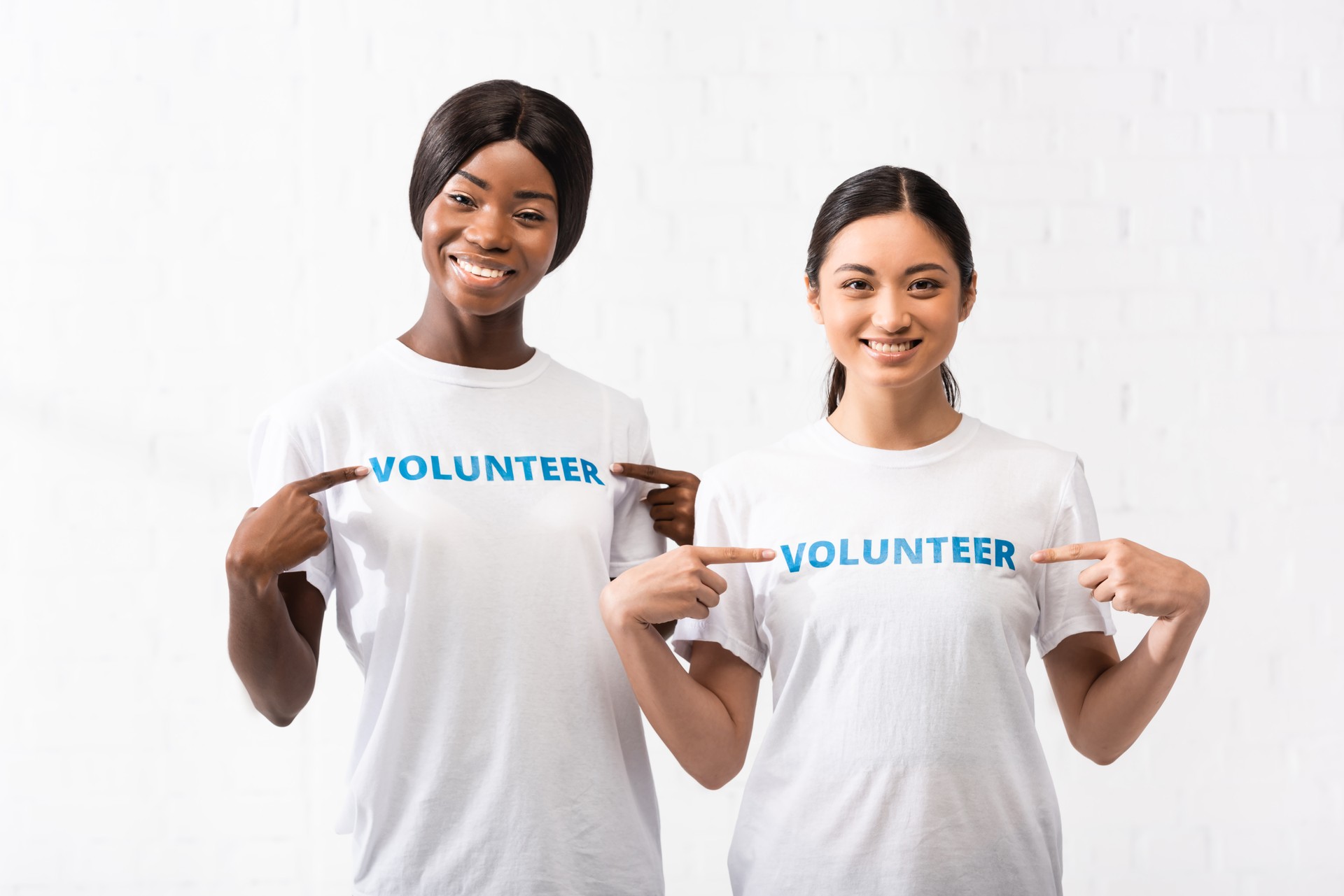 African american and asian volunteers pointing with fingers at t-shirts