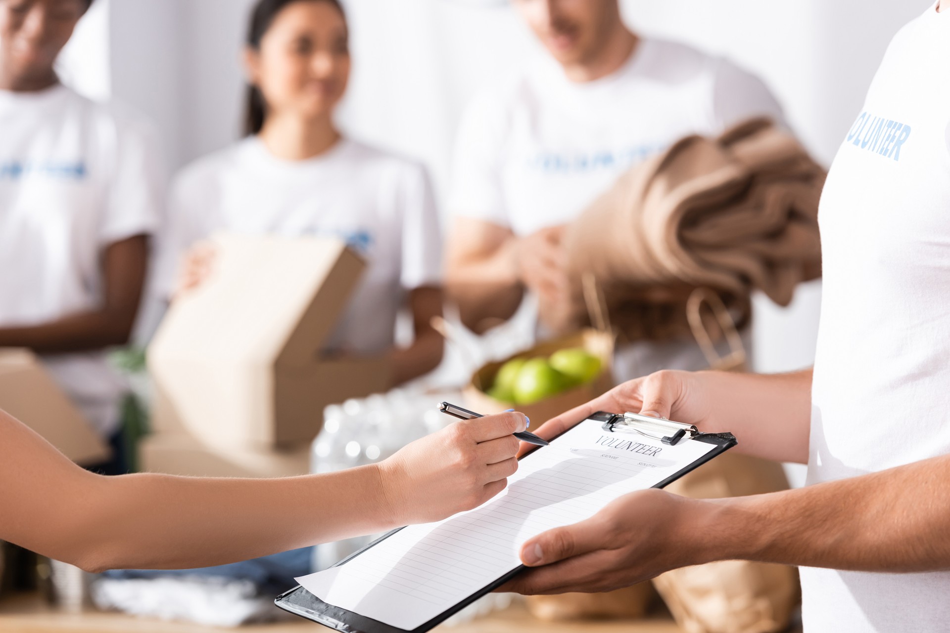 Selective focus of woman writing on clipboard near volunteer in charity center