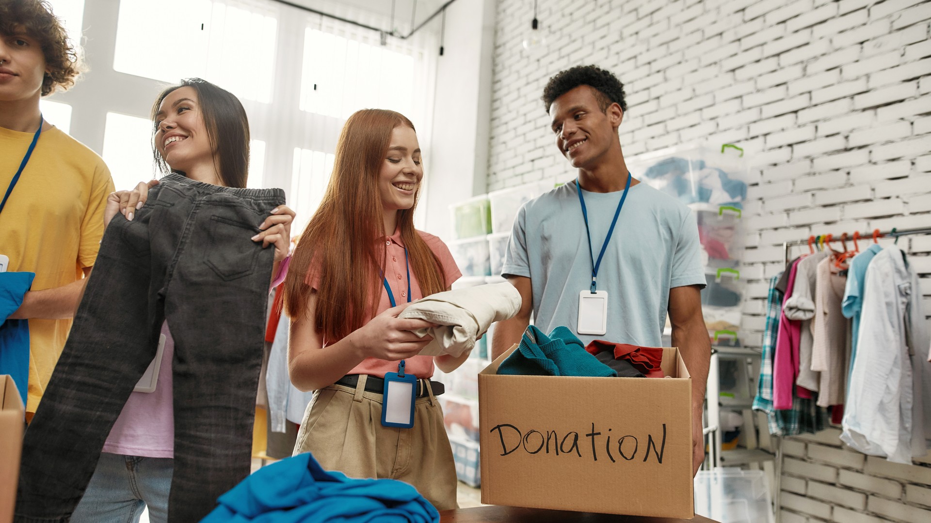 Happy young volunteers sorting, packing clothes in cardboard boxes, Diverse team working together on donation project indoors